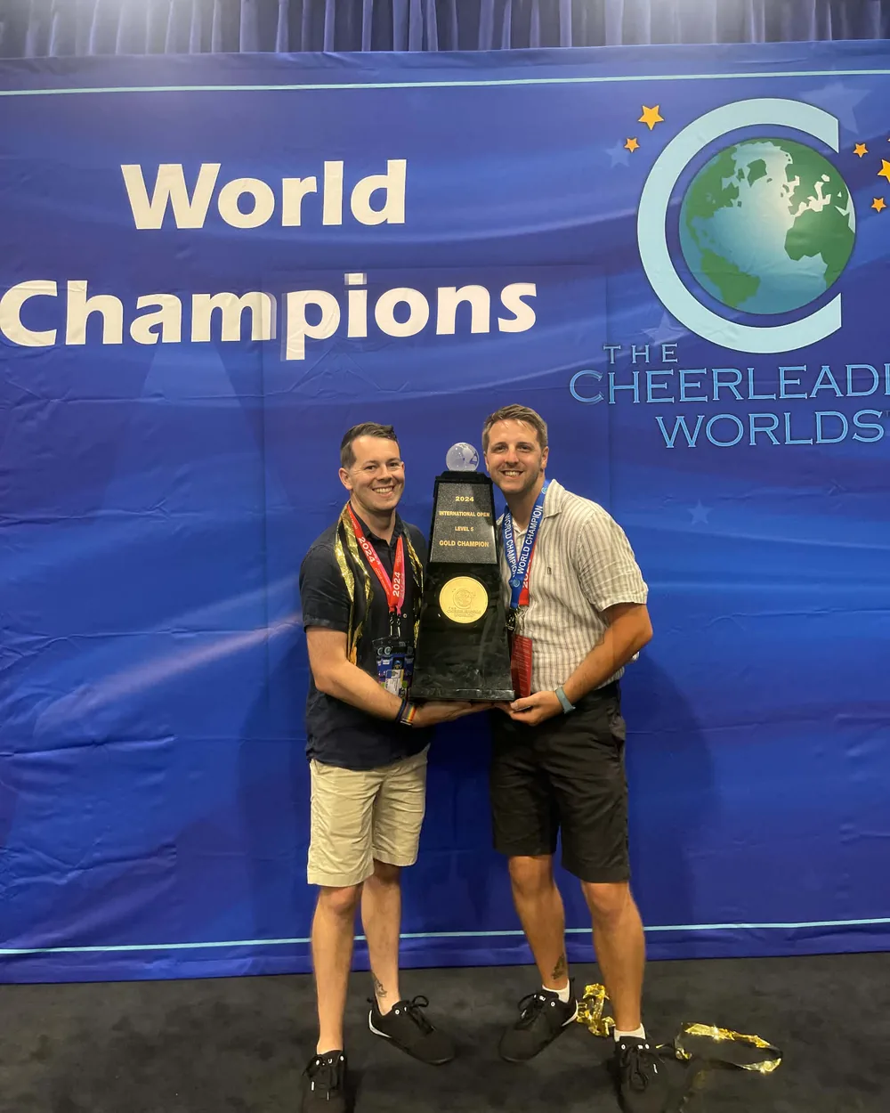 Dan and Brendan holding a 2024 Cheerleading Worlds gold champion trophy